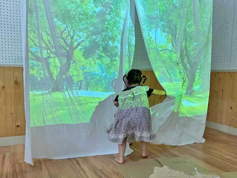 森の映像が映った布に手を伸ばす子ども
