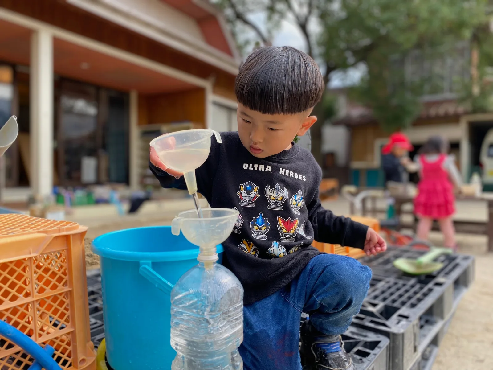 漏斗や容器を使い、水の流れを試す子ども