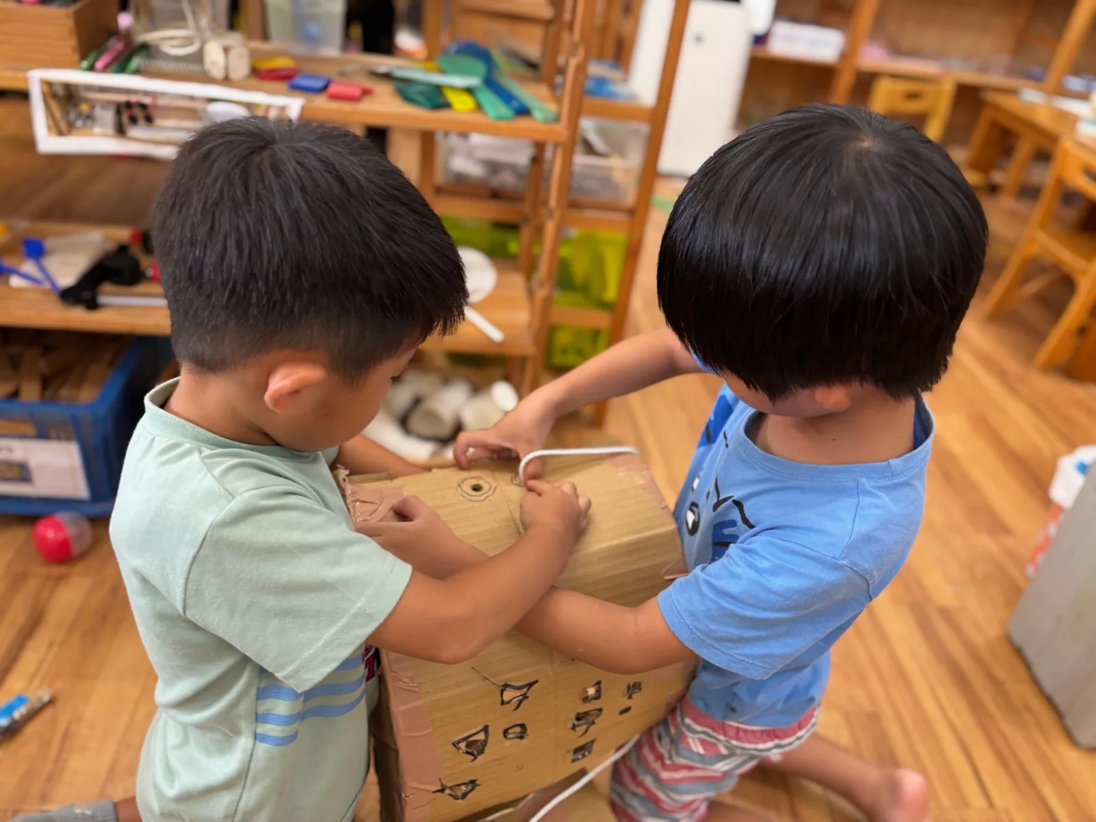 段ボールとひもを使った仕組みを二人で工夫する子どもたち