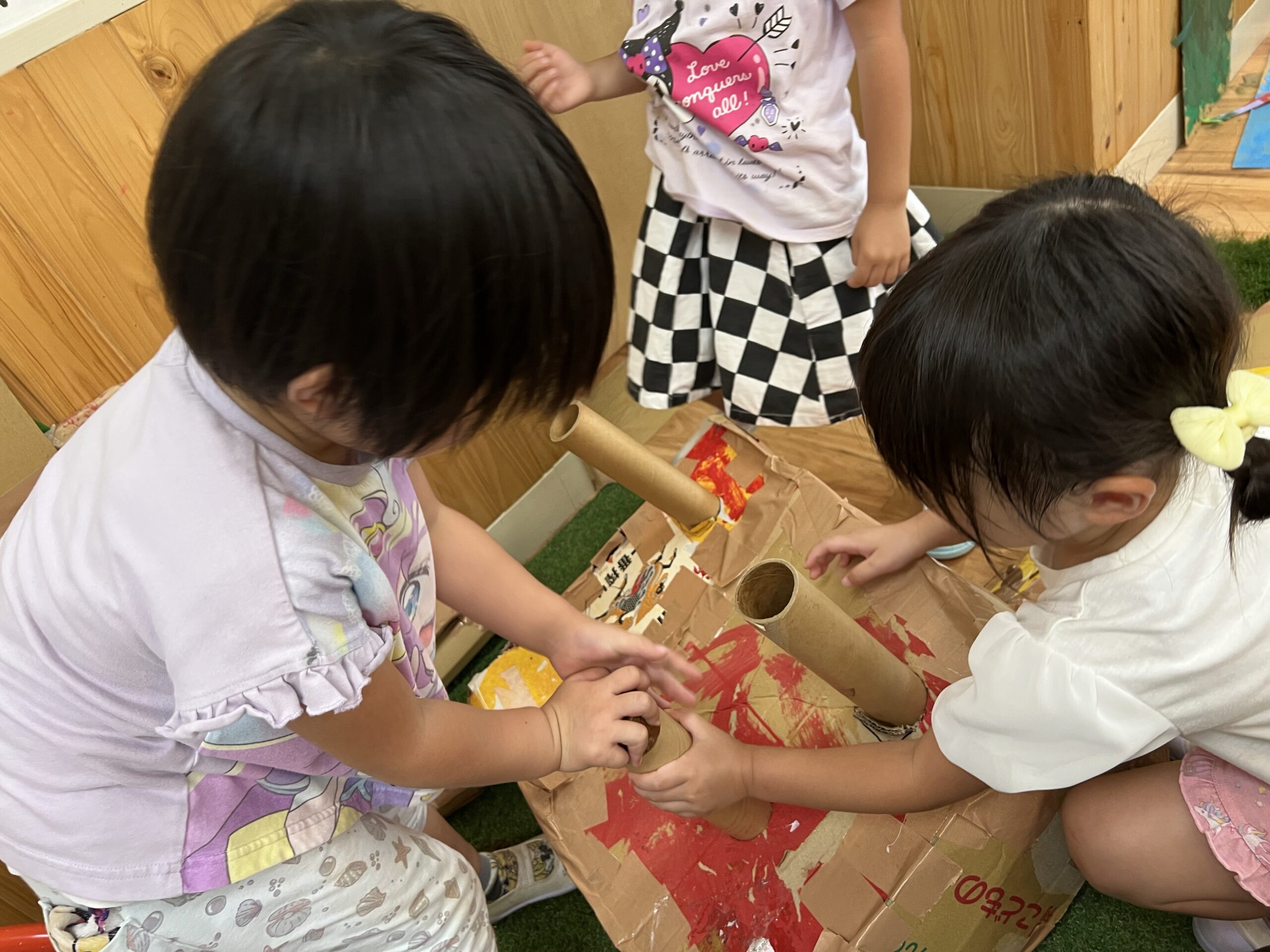 キリンの体に筒の足を取りつけようとする二人の子ども