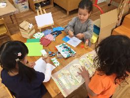 机に広げた紙や描画材料を使って家を作る子どもたち