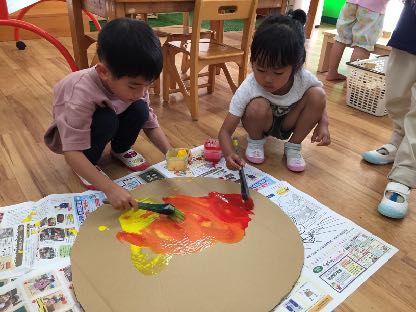 丸い段ボールに赤と黄色の絵の具を塗って太陽を作る子どもたち