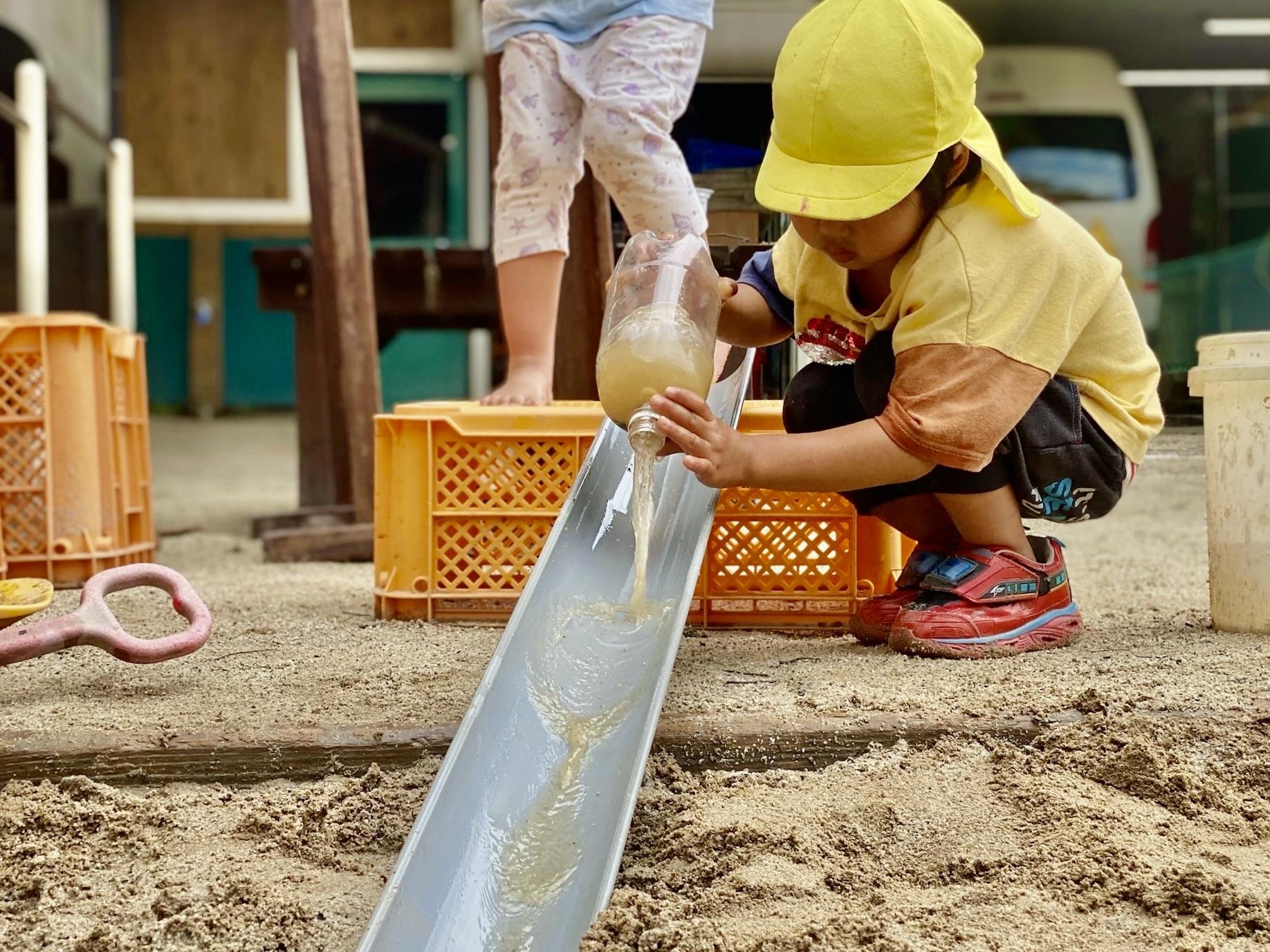 雨どいにペットボトルの水を流す子ども
